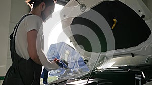 Guy near white auto, male looks in open bonnet, men in backlight,