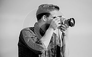 Guy outdoors blue sky background. Handsome blogger guy traveler retro camera. Reporter taking photo. Manual settings