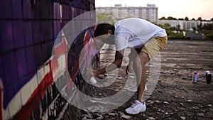 Guy painting graffiti on wall with an aerosol, side view. Talented young graffiti artists painting. Man drawing graffiti