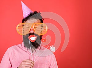 Guy in party hat celebrate, posing with photo props. Hipster in giant sunglasses celebrating. Man with beard on cheerful