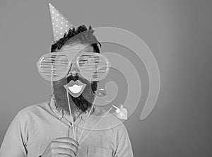 Guy in party hat celebrate, posing with photo props. Hipster in giant sunglasses celebrating. Man with beard on cheerful
