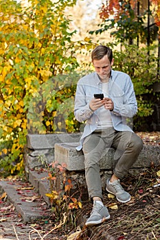 Guy with a phone in casual clothes in the autumn park