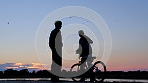 The guy picks up the phone and takes a selfie on the phone at dawn. Silhouette of a man and a teenager with a bicycle being photog