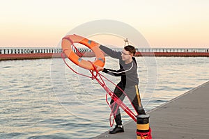 A guy on a pier near the sea throws an orange life buoy into the sea