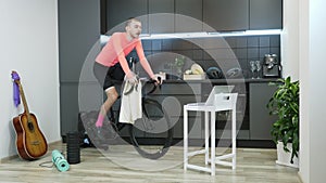 Guy in pink cycling apparel doing fitness exercises on indoor smart cycling trainer staying home during coronavirus pandemic. Youn