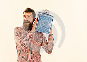 Guy in plaid shirt holds present box near his ear. Surprise and holiday gift concept. Macho with wrapped blue gift