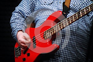 A guy in a plaid shirt with an red electric guitar stands on the recording Studio. The guitarist plays the strings of a musical