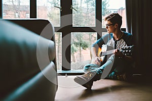 Guy plaing on guitar sits on the floor at home