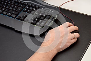 Guy is playing a video game. Close up of a hand lying on a mouse and a black gaming keyboard on a black table. Top view