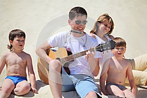 Guy plays guitar and lip accordion with children