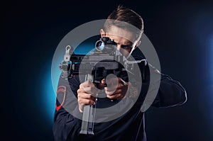 A guy in a police uniform with a short barreled automatic rifle with a telescopic sight takes aim