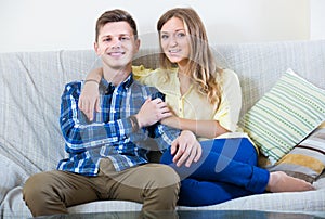 Guy and pretty girl cuddling on sofa indoors