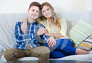 Guy and pretty girl cuddling on sofa indoors