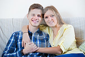 Guy and pretty girl cuddling on sofa indoors