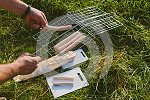 The guy puts sausages on the wire rack. Picnic in nature