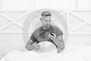 Guy reading sms message in mobile phone while drinking morning tea or coffee in bed, smartphone