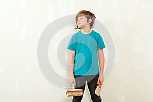 Guy ready to paint the wall at his room. Happy boy holding paint brushes. Son helps parents to paint wall. New house for family