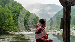 Guy with red jacket looking and thinking with the fog and the river in the nature at the mountain.