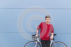 Guy in a red sweatshirt standing with a white bike on the background of a blue wall and looking into the camera