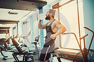 Guy relaxing after workout and hold or drink water from big bottle in gym