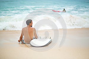 The guy is resting on a sandy tropical beach, after riding a surf. Healthy active lifestyle in summer vocation