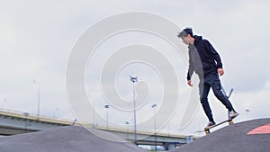 Guy rides skateboard on asphalt waves. Skatepark