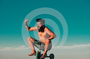 Guy riding childs tricycle. Portrait of a bearded man as a crazy hipster having fun with bicycle outdoors. Excited young