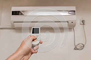 The guy`s hand holds the remote control of the air conditioner. Cooling and temperature control in the room of the house