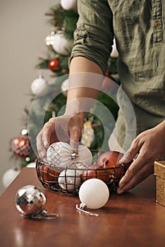 Guy`s hands ornamenting the pine tree with a white ball decoration.