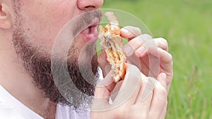 The guy\'s mouth bites a big burger close-up. Snack in nature