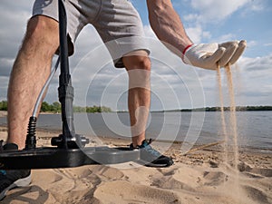 Guy on a sandy coast looking for treasure with a metal detector on a sunny summer day