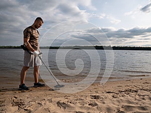 Guy on a sandy coast looking for treasure with a metal detector on a sunny summer day