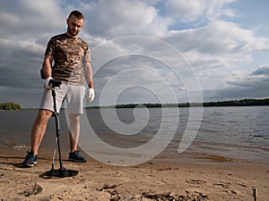 Guy on a sandy coast looking for treasure with a metal detector on a sunny summer day