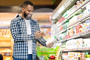 Guy Scanning Product Via Phone Doing Grocery Shopping In Supermarket