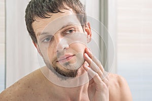 Guy shaved one half of his face and looks in the mirror evaluating the result