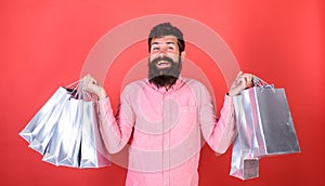 Guy shopping on sales season with discounts. Man with beard and mustache holds shopping bags, red background. Sale and