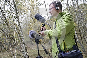 The guy with Shotgun Condenser Microphone and headphones is recording the sounds of nature.