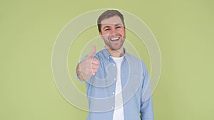 The guy shows his thumb up, he is wearing a denim shirt on an olive background.