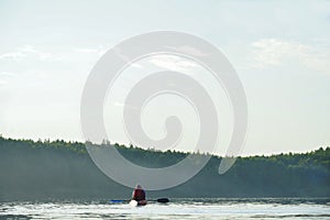 The guy sits in a boat on the lake with paddles. fog is rising over the lake