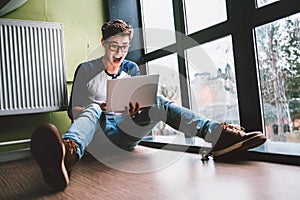 Guy sits on the floor and watches something impressing in laptop