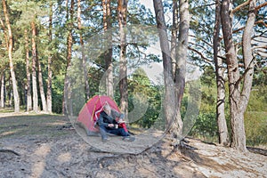 Guy sits near the tent in the forest