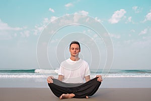 The guy sits on the seashore in the lotus position and meditates.