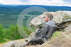 The guy sits on the top of the mountain and enjoys the beautiful view of nature