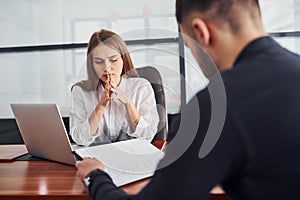 Guy sitting with documents. Woman and man in formal clothes working together indoors in the office by table