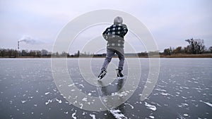 Guy skating on frozen river at cloudy day. Young man shod in figure skates sliding on ice surface outdoor. Sportsman