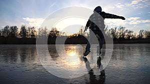 Guy skating on frozen river during sunset time. Young man shod in figure skates sliding on ice. Sun is reflecting on