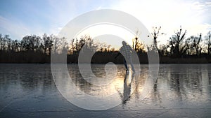 Guy skating on frozen river during sunset time. Young man shod in figure skates sliding on ice. Sun is reflecting on