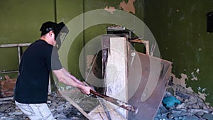 A guy smashes an old closet in an abandoned house with a baseball bat