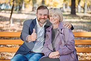 The guy with a smile hugs my mother in an autumn park on a bench