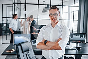 Guy standing in front of people. Team of stockbrokers works in modern office with many display screens